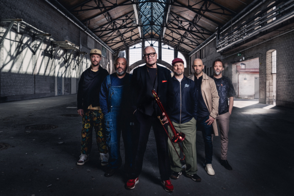 Eine Musikgruppe steht in einer großen, leeren Halle mit hohen Decken und Glasdach.