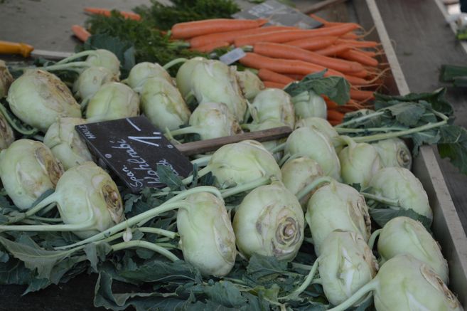 Nahaufnahme von Kohlrabi und Karotten auf einem Marktstand.