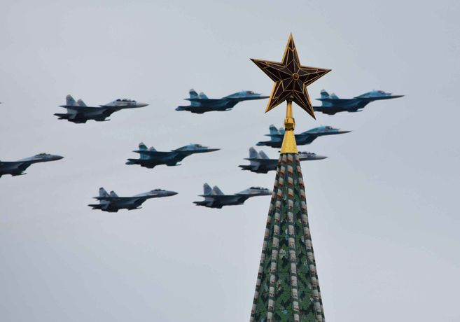 Kampfjets am Himmel, im Vordergrund die Spitze eines Turms auf der ein goldener Stern steht.