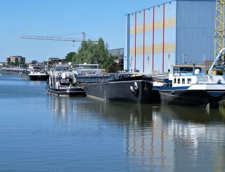 Binnenschiffe liegen an einem Kanal vor Anker, mit einem großen Lagerhaus im Hintergrund.