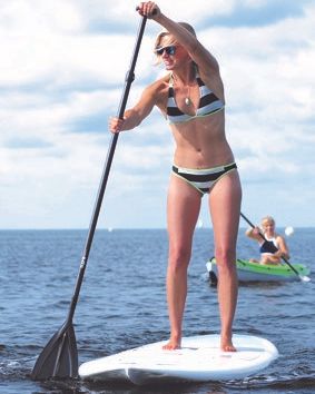 Frau auf einem Stand-Up-Paddle-Board auf dem Wasser, im Hintergrund eine Person in einem Kajak.