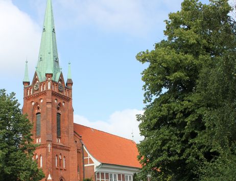 Kirche St. Nikolai Moorfleet mit rotem Backstein und grünem Turm, umgeben von Bäumen.