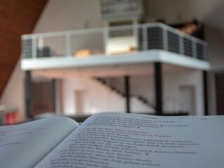 Ein aufgeschlagenes Buch im Vordergrund, im Hintergrund eine Empore mit Geländer in einem modernen Kirchenraum.
