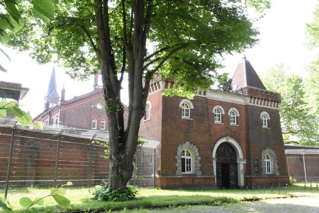 Ein Torhaus mit zwei kleinen Türmen, im Vordergrund ein Baum