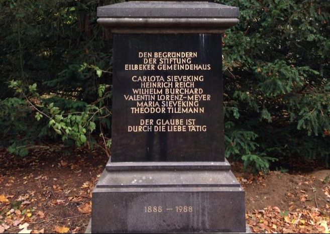 Ein schwarzer Gedenkstein mit goldener Inschrift im Jacobipark, umgeben von Bäumen und Laub.