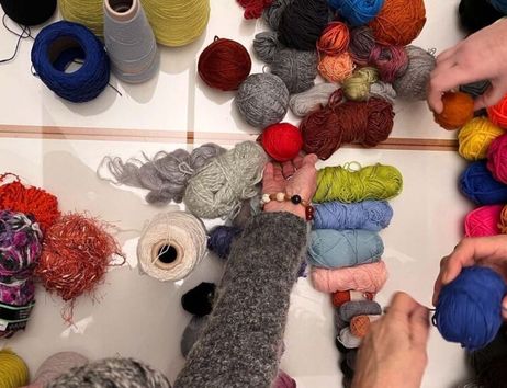 Hände ordnen bunte Wollknäuel auf einem Tisch; passend zum Titel „Die neue Masche - Häkelgespräche im Altonaer Museum“.
