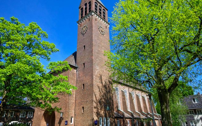 Backsteinkirche mit hohem Turm und grünen Bäumen im Vordergrund.