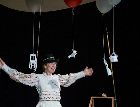 Eine Person in traditioneller Kleidung steht auf einer Bühne mit schwebenden Papierfiguren und Ballons.