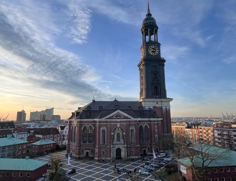 Die Kirche St. Michaelis in Hamburg bei Sonnenuntergang, mit der Elbphilharmonie im Hintergrund.