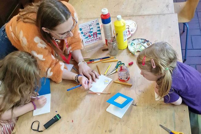 Eine Frau und zwei Kinder sitzen an einem Tisch und basteln mit Farben und Papier.