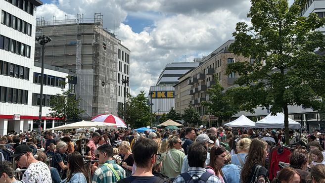 Viele Menschen im unteren Teil des Bildes, befinden sich auf einem Flohmarkt draußen in der Sonne. Im Hintergrund sind Gebäude zu sehen und ganz am hinten im Bilde der IKEA in der Neuen Grossen Bergstrasse in Altona.