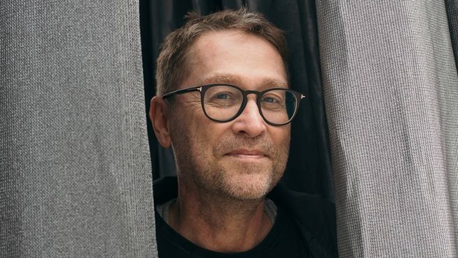 Ein Mann mit Brille schaut zwischen zwei Vorhängen hervor.