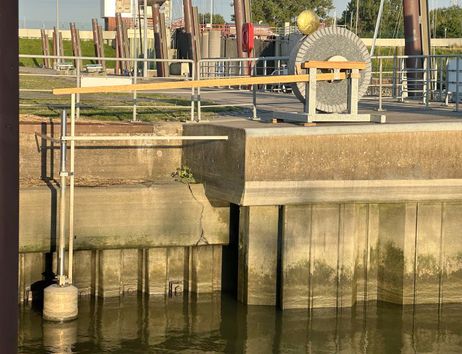 Ein Schwimmer an einer Betonmauer in einem Hafenbereich mit Geländer und mechanischer Vorrichtung im Hintergrund.