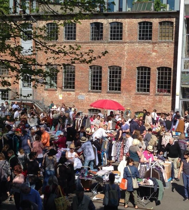 Menschenmenge auf einem Flohmarkt vor einem Backsteingebäude.