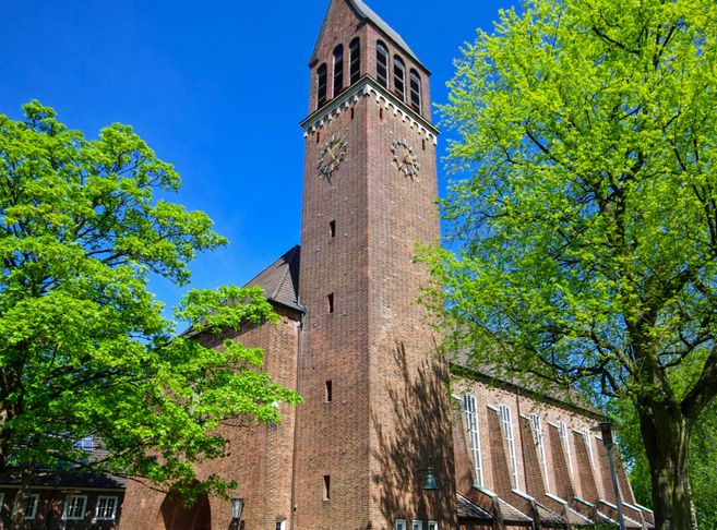 Backsteinkirche mit Turm und grünen Bäumen im Vordergrund.