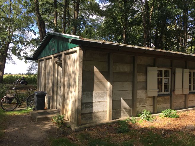 Eine Hütte im im Wald mit grünem Dach, im Hintergrund eine Landstraße