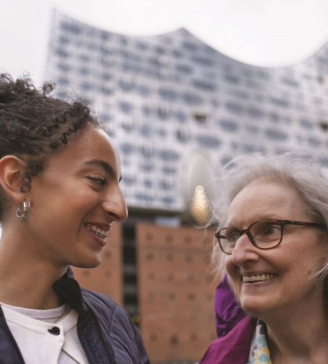 Zwei Frauen lächeln sich vor der Elbphilharmonie in Hamburg an.