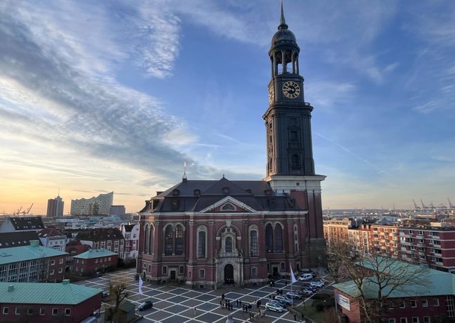 Die Kirche St. Michaelis in Hamburg bei Sonnenuntergang, mit der Elbphilharmonie im Hintergrund.