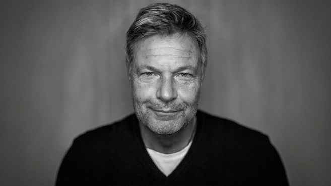Schwarz-weiß Porträt eines lächelnden Mannes mit Bart und kurzen Haaren.