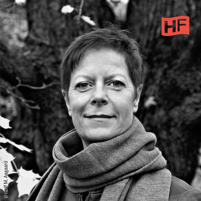 Schwarz-weiß Porträt einer Person mit kurzem Haar und Schal vor einem Baum.