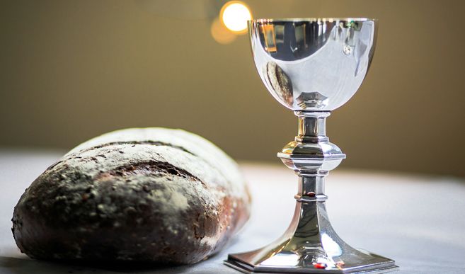 Ein silberner Kelch steht neben einem Laib Brot auf einem Tisch.