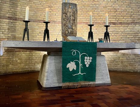 Altar in der Paul-Gerhardt-Kirche mit Kerzen und einem grünen Tuch mit Weinrebenmotiv.