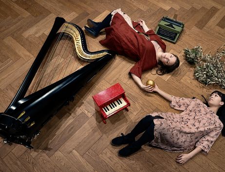 Die beiden Musikerinnen von Temarioto liegen auf dem Parkettboden, ihre Instrumente um einander drapiert. Sie halten gemeinsam eine goldene Kugel.