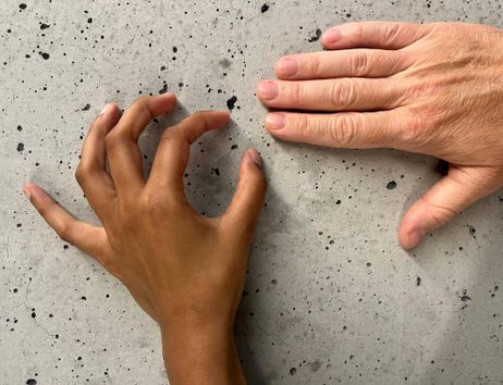 Das BIld zeigt zwei Hände. Oben im Rechten Bildrandliegt eine glatte Hand auf einer Oberfläche aus Beton. Unten mittig ragt eine linke Hand ins Bild hinein. Die Finger formen jeweils angedeutete Kreise.