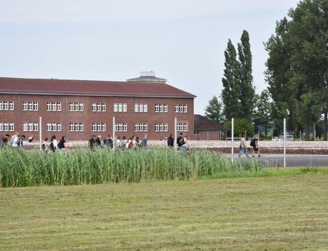 Das Gelände der Gedenkstätte, ein Klinkerhaus, im Vordergrund eine Wiese und eine Gruppe Menschen