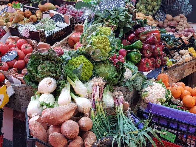 Ein Marktstand mit frischem Obst und Gemüse, darunter Tomaten, Paprika, Fenchel, Blumenkohl und Süßkartoffeln.