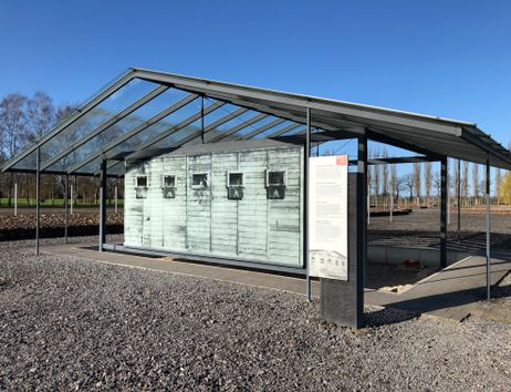 Ein offenes Metallgerüst in Form eines Hauses auf Schotterboden. Darin sind Darstellungen von der Außenwand des Arrestbunkers.