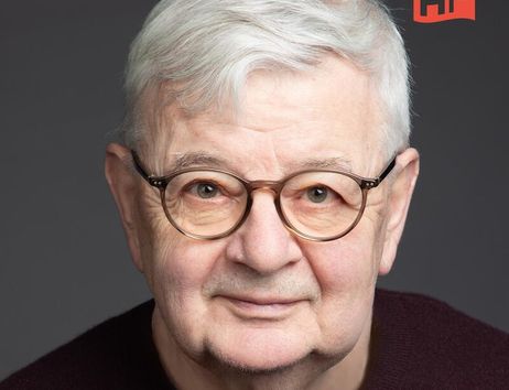 Porträt eines älteren Mannes mit Brille und grauen Haaren vor grauem Hintergrund.