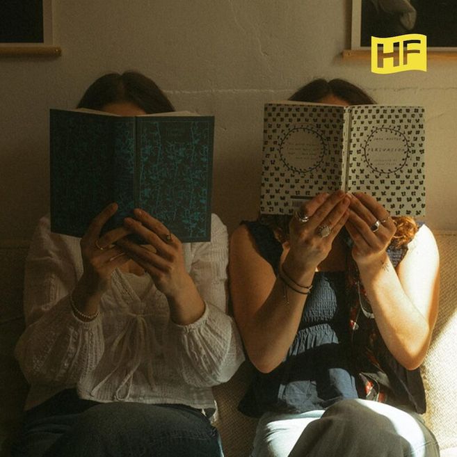 Zwei Personen sitzen auf einem Sofa und lesen Bücher, deren Cover ihre Gesichter verdecken. Oben rechts ist ein gelbes Logo mit den Buchstaben 'HF'.