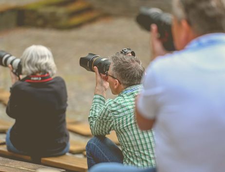 Drei Personen mit Kameras bei einem Fotoworkshop im Freien.