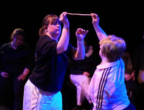Zwei Performer:innen des Klabauter Theaters bewegen sich in bläulichem Licht und halten gemeinsam einen kleinen Ast in der Luft. 