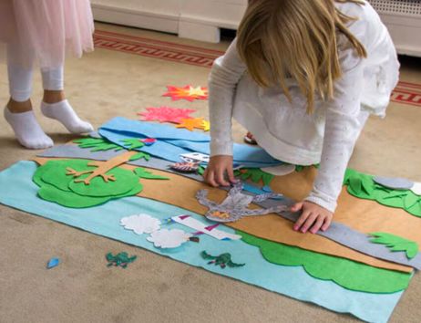 Zwei Kinder spielen mit Filzfiguren auf einem Teppich.