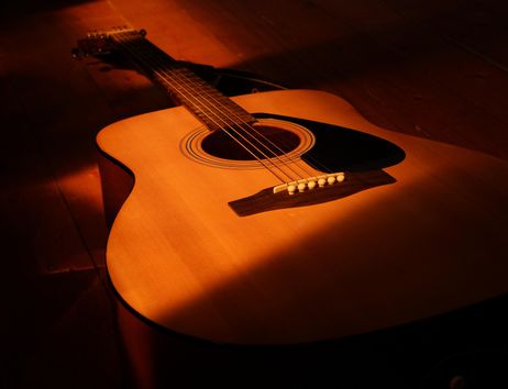 Eine Akustikgitarre liegt auf einem Holzboden im warmen Licht.