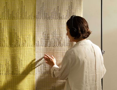 Zu sehen ist eine junge Frau, die ein großes, mit Sensoren versetztes Textil berührt und dabei große Kopfhörer trägt.