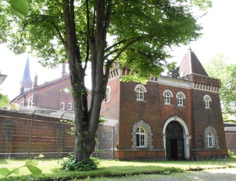 Ein Torhaus mit zwei kleinen Türmen, im Vordergrund ein Baum