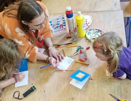 Eine Frau und zwei Kinder sitzen an einem Tisch und basteln mit Farben und Papier.