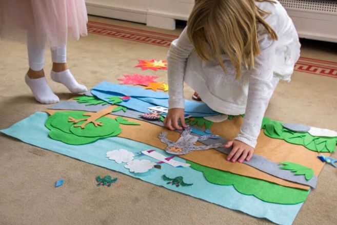 Zwei Kinder spielen mit Filzfiguren auf einem Teppich.