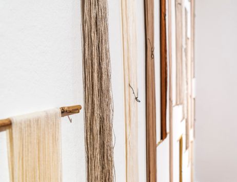 Nahaufnahme von Garnsträngen in verschiedenen Farben, die an einer weißen Wand hängen.