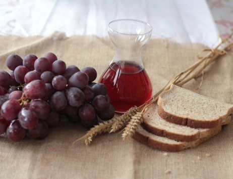 Ein Stillleben mit roten Trauben, einem Krug mit rotem Saft und drei Brotscheiben auf einem Jutetuch.