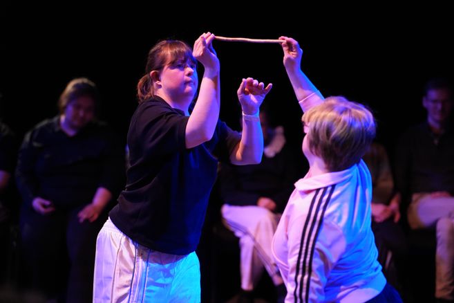 Zwei Performer:innen des Klabauter Theaters bewegen sich in bläulichem Licht und halten gemeinsam einen kleinen Ast in der Luft. 