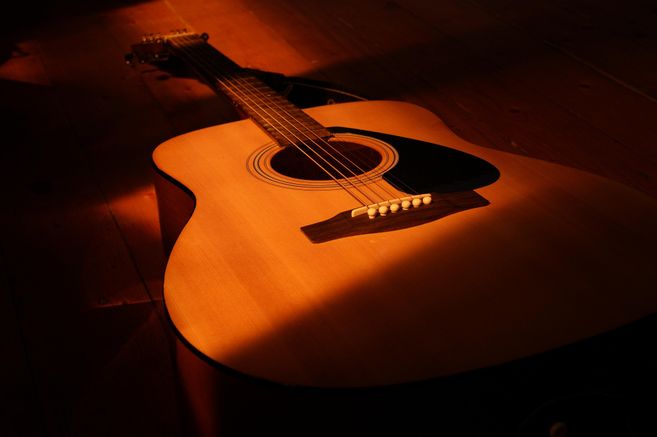 Eine Akustikgitarre liegt auf einem Holzboden im warmen Licht.