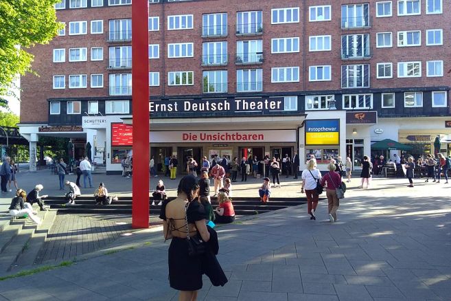Menschen versammeln sich vor dem Ernst Deutsch Theater in Hamburg bei sonnigem Wetter.