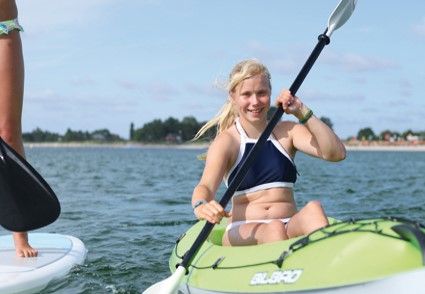 Eine junge Frau paddelt in einem Kajak auf dem Wasser, während eine andere Person auf einem Stand-Up-Paddle-Board steht.