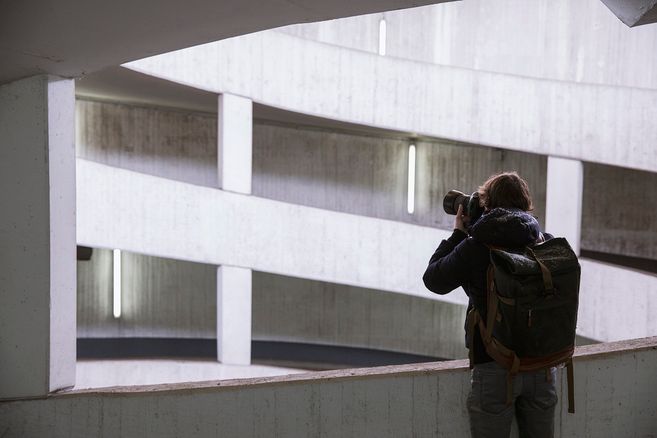 Ein Fotograf mit Rucksack fotografiert in einem spiralförmigen Parkhaus.