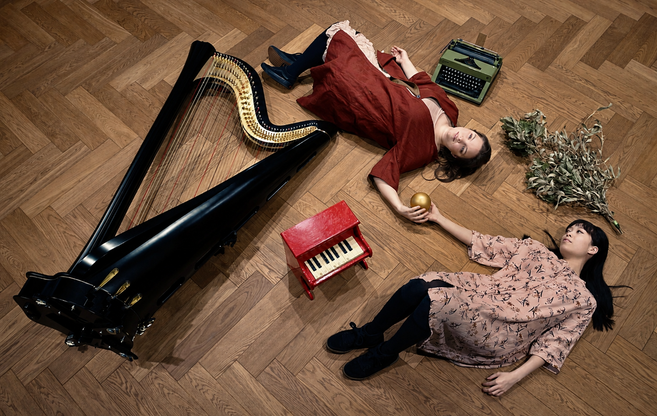 Die beiden Musikerinnen von Temarioto liegen auf dem Parkettboden, ihre Instrumente um einander drapiert. Sie halten gemeinsam eine goldene Kugel.