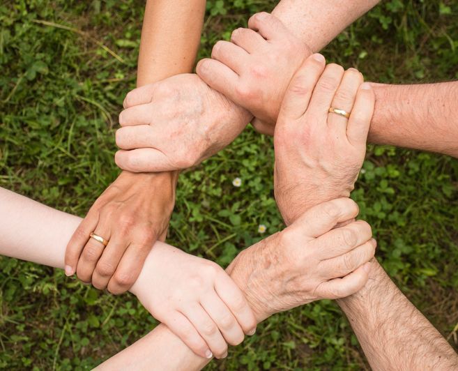 Sechs Hände, die sich im Kreis am Handgelenk umfassen